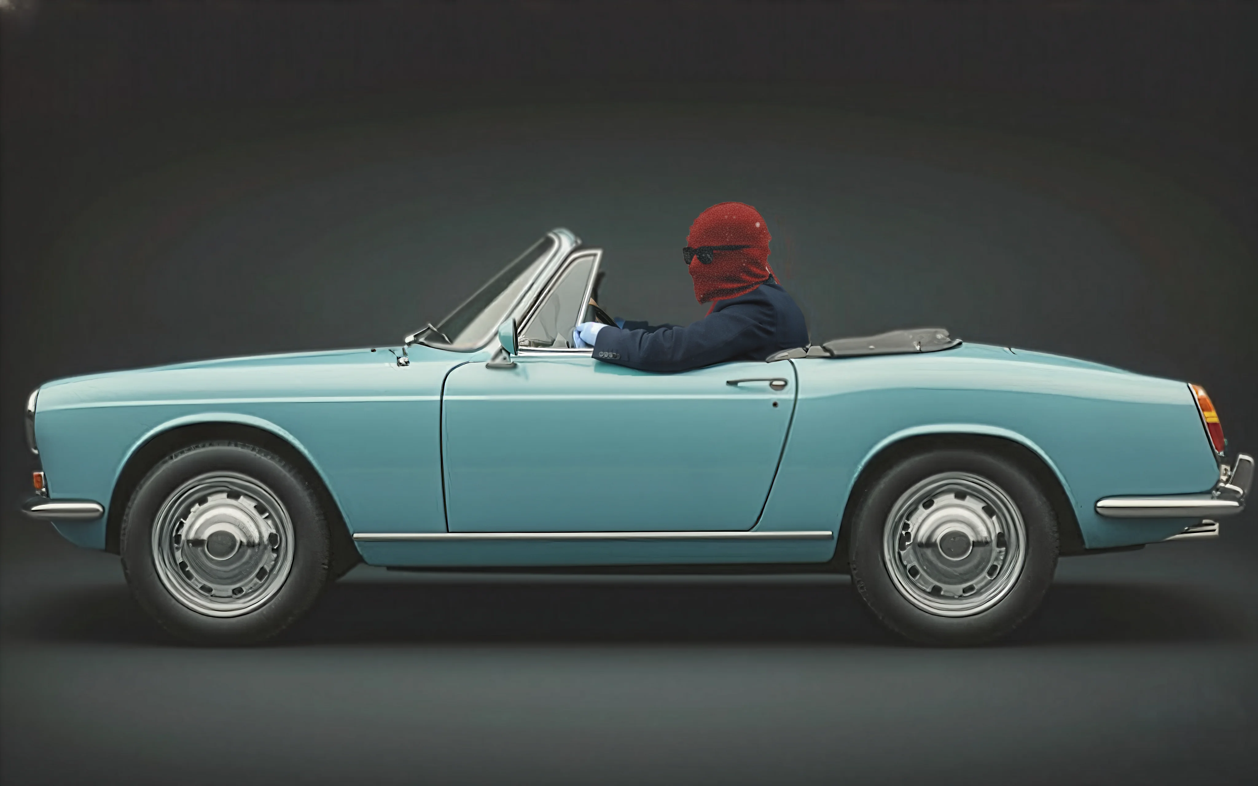 A person in a red ski mask and blue suit driving a vintage convertible car.